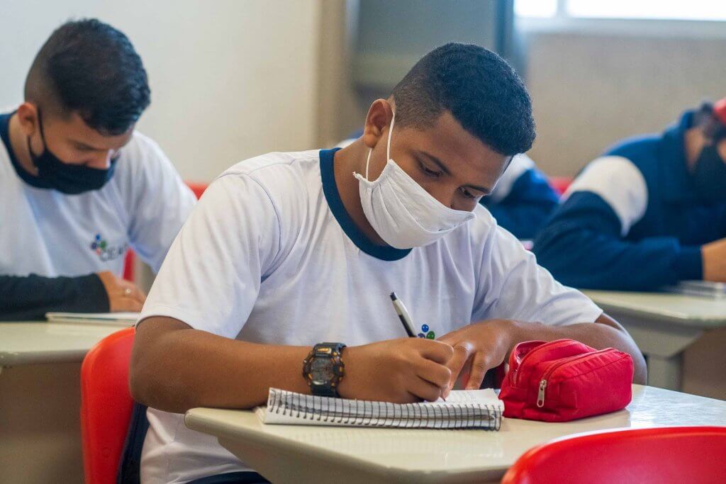 Garoto, em sala de aula, escrevendo em seu caderno. Ele está recebendo a metodologia da instituição que está cumprindo o "S" do ESG.