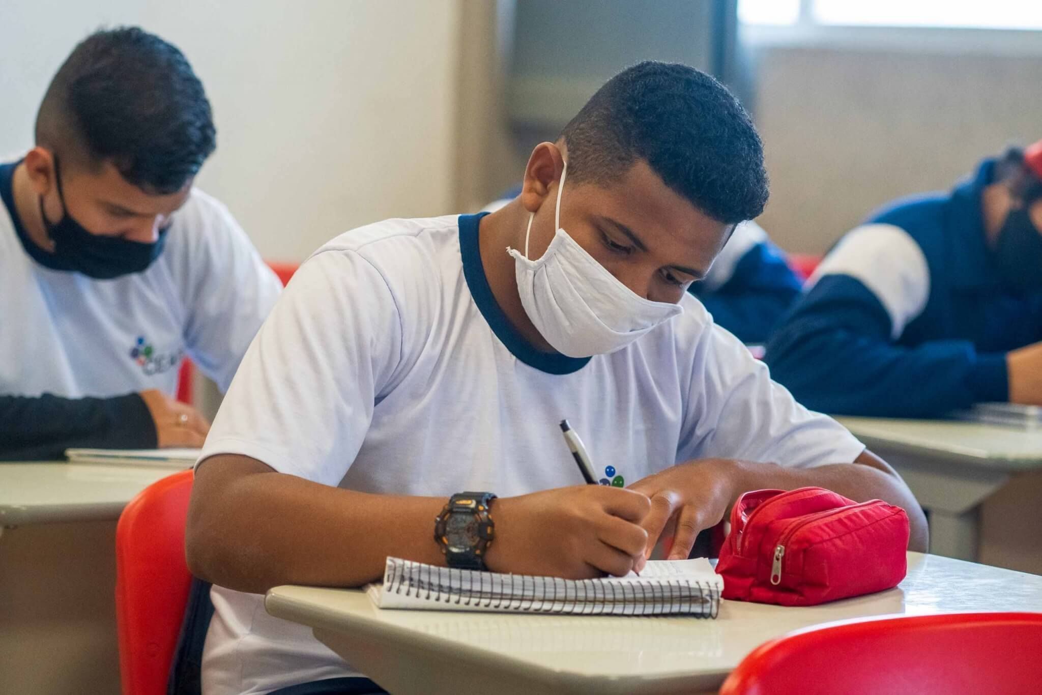 Garoto, em sala de aula, escrevendo em seu caderno. Ele está recebendo a metodologia da instituição que está cumprindo o 